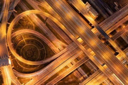 Aerial view of a complex highway interchange illuminated at night with warm golden lights.