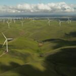 Aerial view of numerous wind turbines across rolling green hills under a cloudy sky.