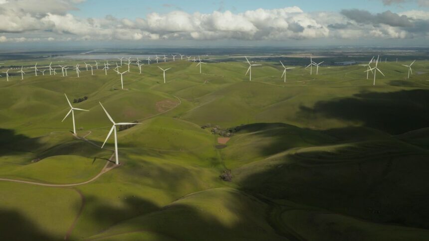 Aerial view of numerous wind turbines across rolling green hills under a cloudy sky.
