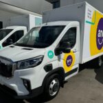 Two white ANC electric delivery trucks parked outside a building.