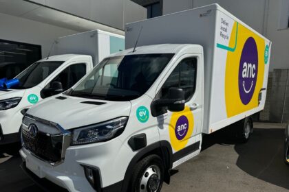 Two white ANC electric delivery trucks parked outside a building.