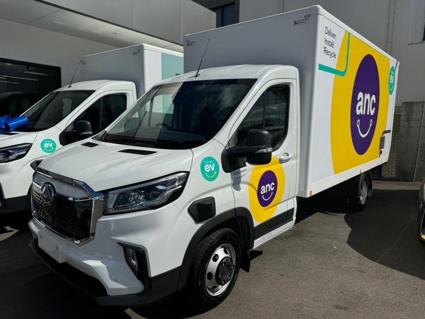 Two white ANC electric delivery trucks parked outside a building.
