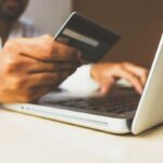 A person holds a credit card while typing on a laptop.
