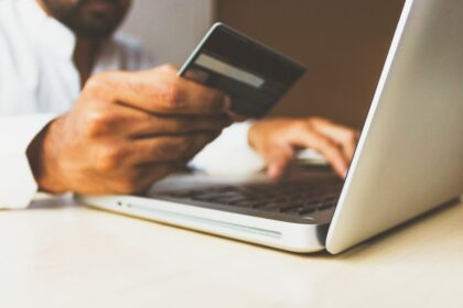 A person holds a credit card while typing on a laptop.