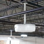 A white, circular industrial sensor mounted to an open ceiling.