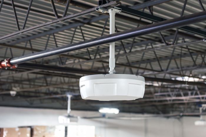A white, circular industrial sensor mounted to an open ceiling.