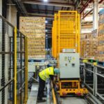 A worker in a high-visibility vest operates machinery in a modern, automated warehouse.