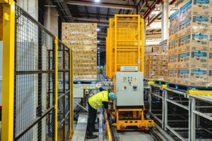 A worker in a high-visibility vest operates machinery in a modern, automated warehouse.