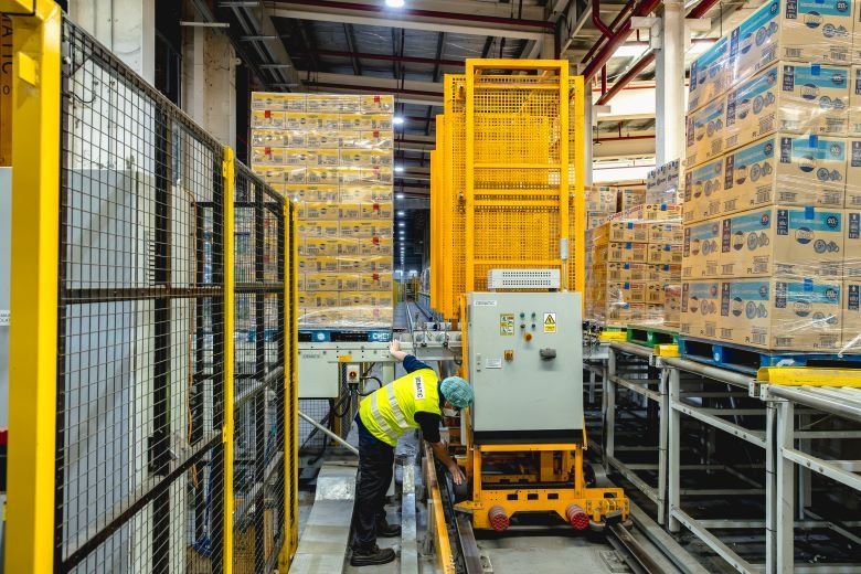 A worker in a high-visibility vest operates machinery in a modern, automated warehouse.