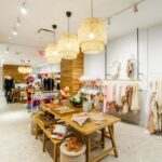 A bright boutique filled with hanging light fixtures, clothing racks, and wooden display tables.