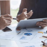 Business professionals analyzing financial charts and data on a tablet during a meeting.