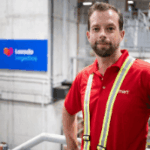 A man in a red work shirt standing in a Lazada logistics warehouse.