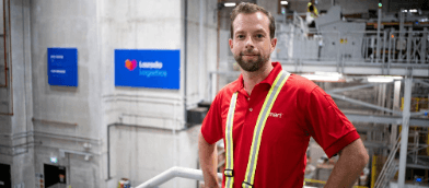 A man in a red work shirt standing in a Lazada logistics warehouse.