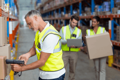 Warehouse workers wearing safety vests scanning items and carrying boxes in a storage facility.