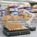 Robotic arm placing a cardboard box on an automated pallet in a warehouse.