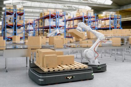 Robotic arm placing a cardboard box on an automated pallet in a warehouse.