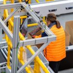 Warehouse worker in a high-visibility vest packing items into a cardboard box.