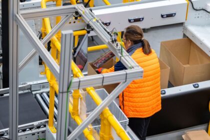 Warehouse worker in a high-visibility vest packing items into a cardboard box.