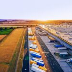 Aerial view of a large logistics warehouse with many trucks and containers at sunset.