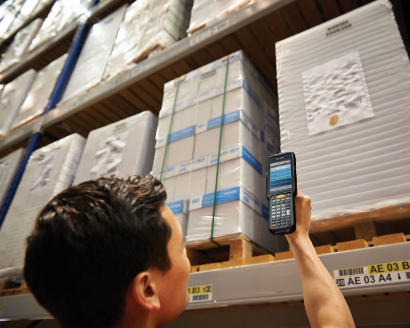 Warehouse worker using a handheld scanner to check inventory on high storage shelves.