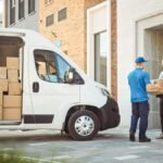 A delivery worker hands a package to a customer outside a modern building.