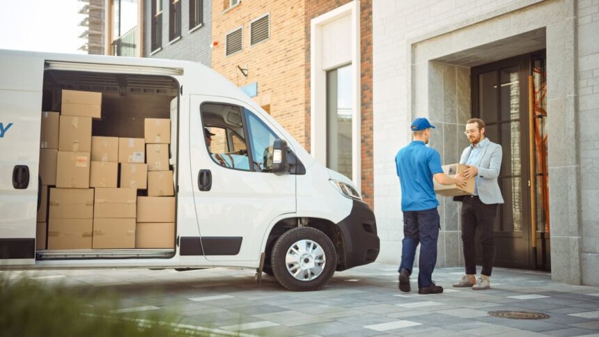 A delivery worker hands a package to a customer outside a modern building.