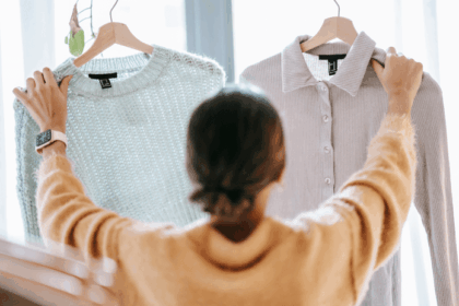 A person in a yellow sweater comparing two shirts hanging on hangers.