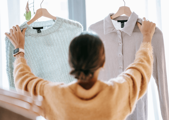 A person in a yellow sweater comparing two shirts hanging on hangers.