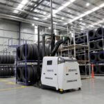 A Dematic automated forklift moving stacks of tires in a large warehouse.