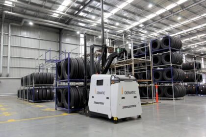 A Dematic automated forklift moving stacks of tires in a large warehouse.