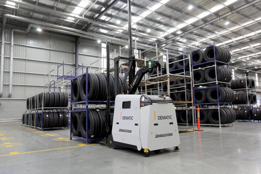 A Dematic automated forklift moving stacks of tires in a large warehouse.