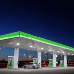 A silver car parked at a gas station under a bright canopy at dusk.