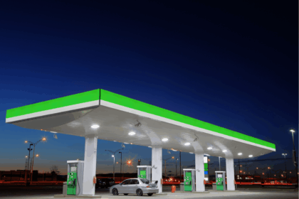 A silver car parked at a gas station under a bright canopy at dusk.