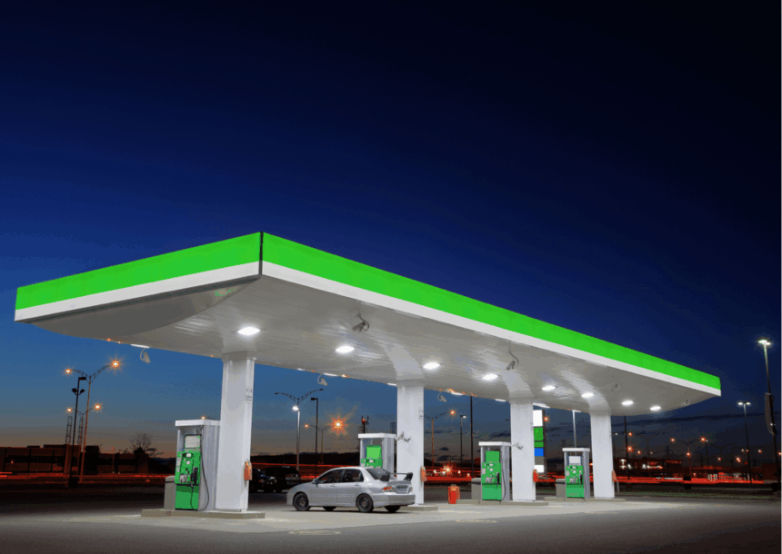 A silver car parked at a gas station under a bright canopy at dusk.