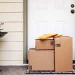 Packages and envelopes left at a front door on a welcome mat.