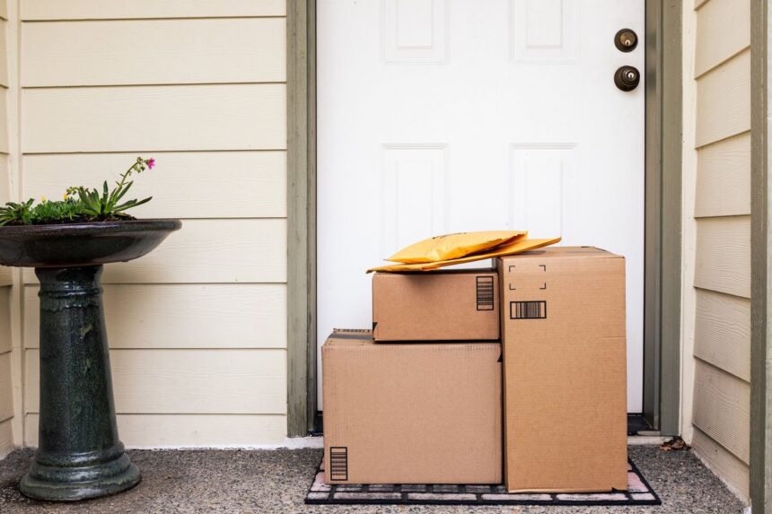 Packages and envelopes left at a front door on a welcome mat.