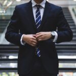 A man in a professional suit adjusting his tie in a modern office building.