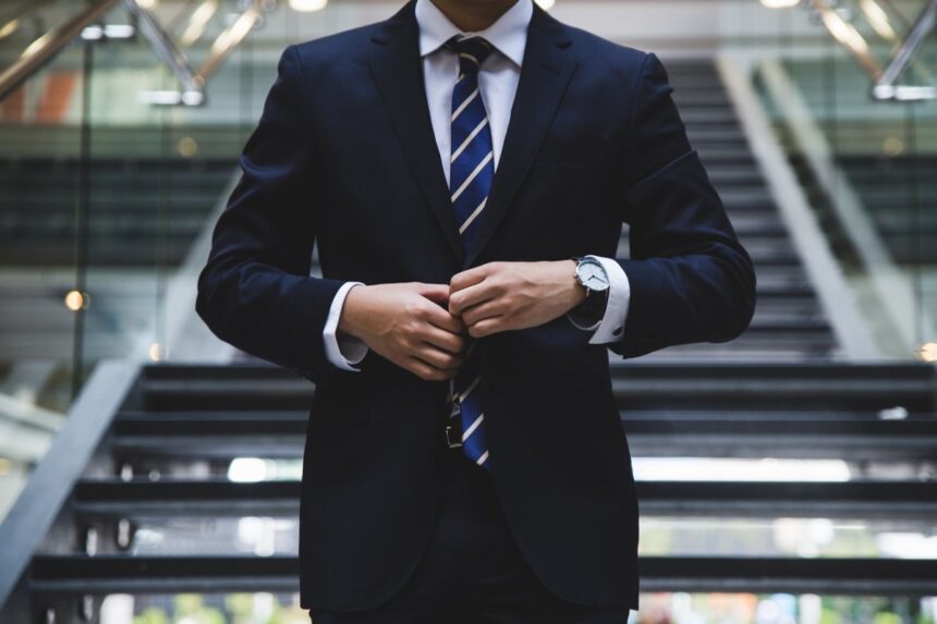 A man in a professional suit adjusting his tie in a modern office building.