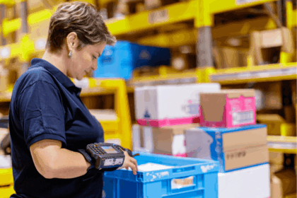 Warehouse worker using a wrist-mounted scanner to process a blue plastic crate.