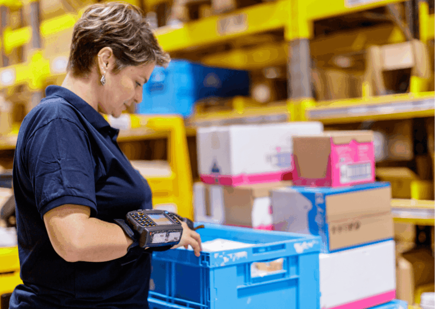 Warehouse worker using a wrist-mounted scanner to process a blue plastic crate.