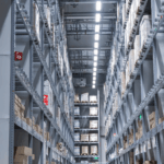 A symmetrical view down a narrow aisle between high industrial storage warehouse racks.