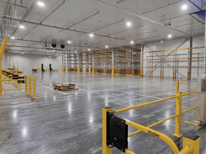 Large, modern, empty warehouse with concrete floors, yellow safety railings, and high industrial racking.