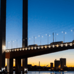 The West Gate Bridge in Melbourne illuminated against a vibrant sunset sky.