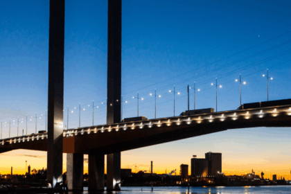 The West Gate Bridge in Melbourne illuminated against a vibrant sunset sky.