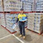 A warehouse worker standing between pallets of Viva paper towels holding two packages.
