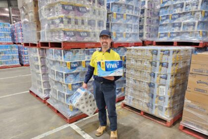 A warehouse worker standing between pallets of Viva paper towels holding two packages.