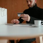 A man in a black turtleneck paying with a credit card on his tablet.