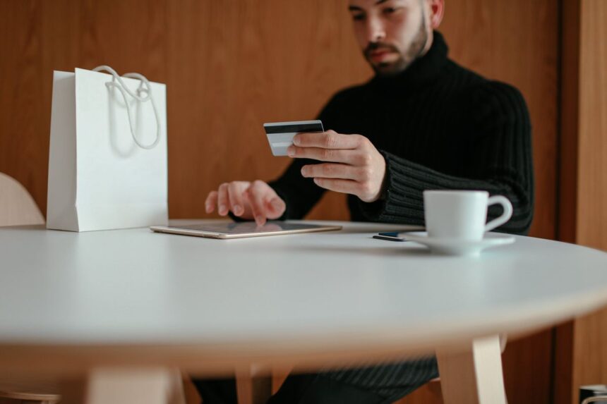 A man in a black turtleneck paying with a credit card on his tablet.