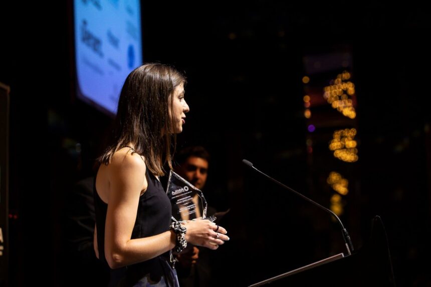 A woman in a black dress stands at a podium holding an award.