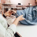 A customer and shop assistant handling a blue garment on a hanger at checkout.